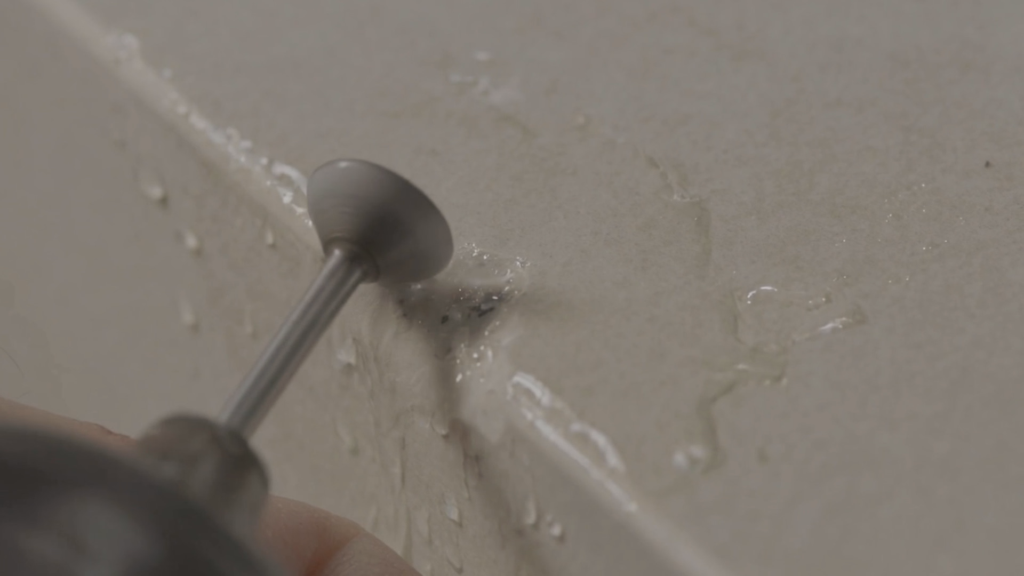 Close-up of a rotary grinding tool being used to smooth and prepare a chipped countertop edge during a technical surface repair process.