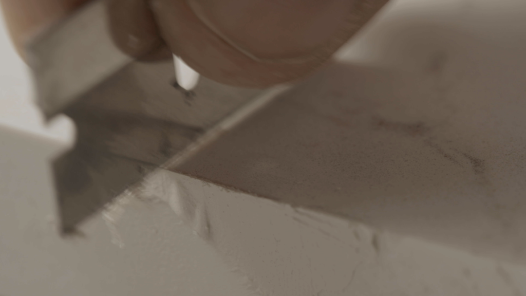 An extreme close-up of a razor blade scraping away excess cured adhesive compound to level the repaired countertop edge with the surface.