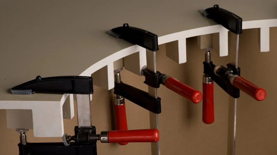 Close-up of clamps holding curved quartz countertop pieces during fabrication.