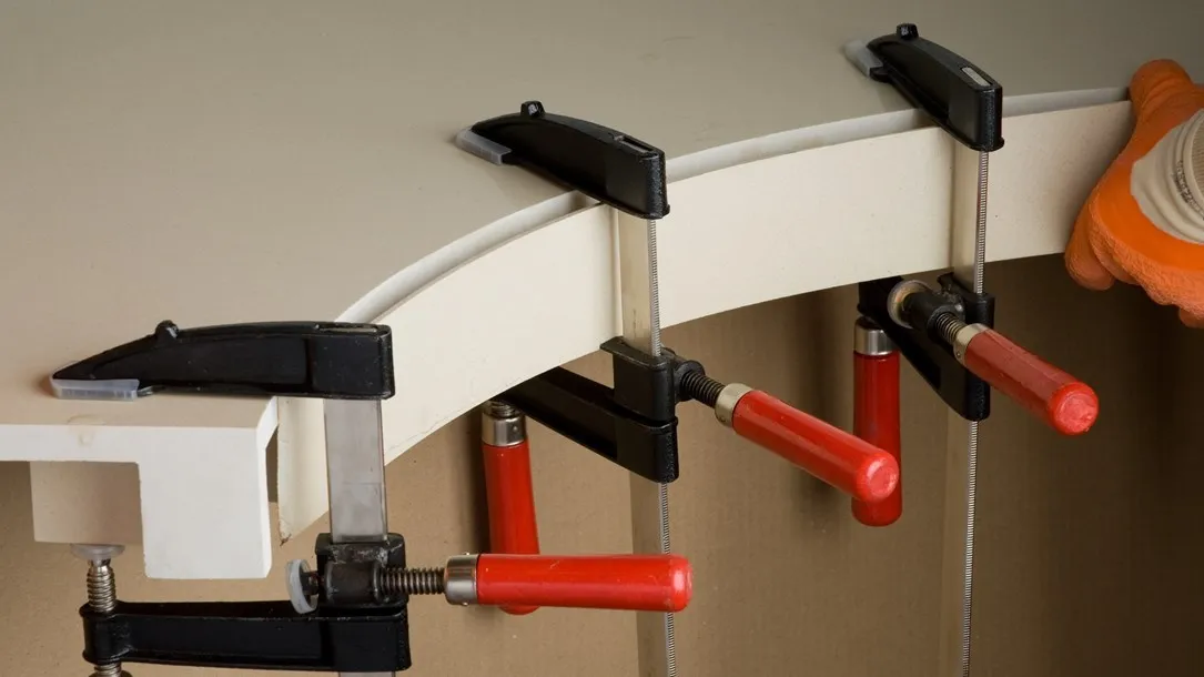 Fabricator shaping a curved Caesarstone quartz surface with clamps and water during the thermoforming process.