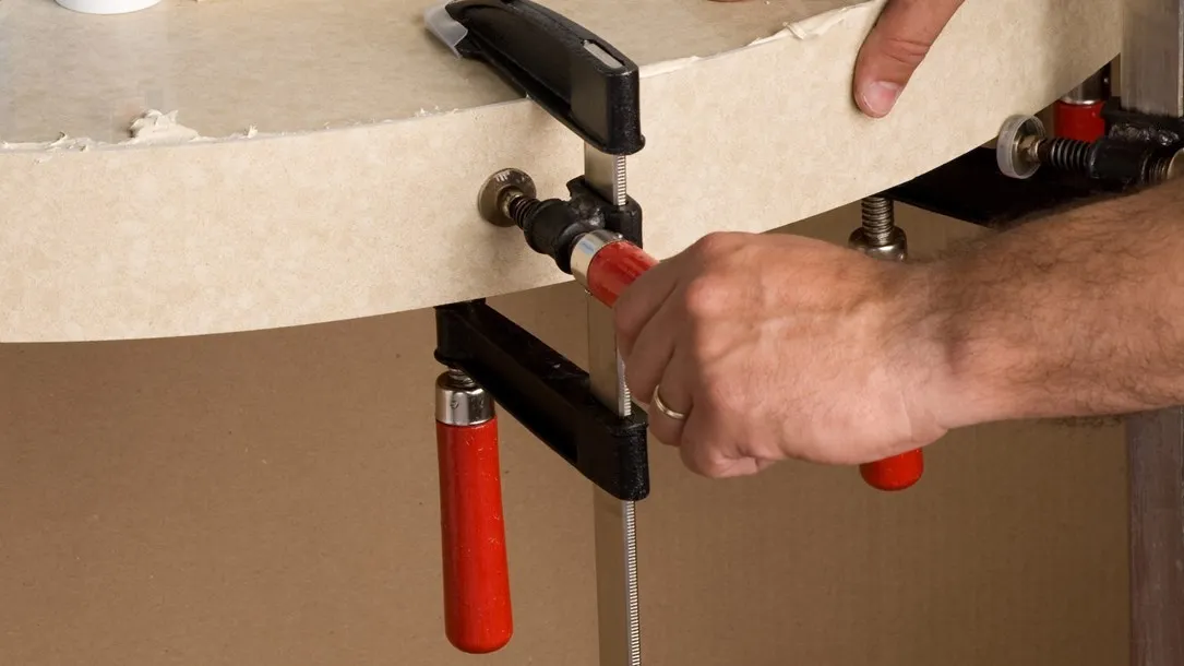 Fabricator applying adhesive to a curved Caesarstone quartz surface held by clamps during the thermoforming process.
