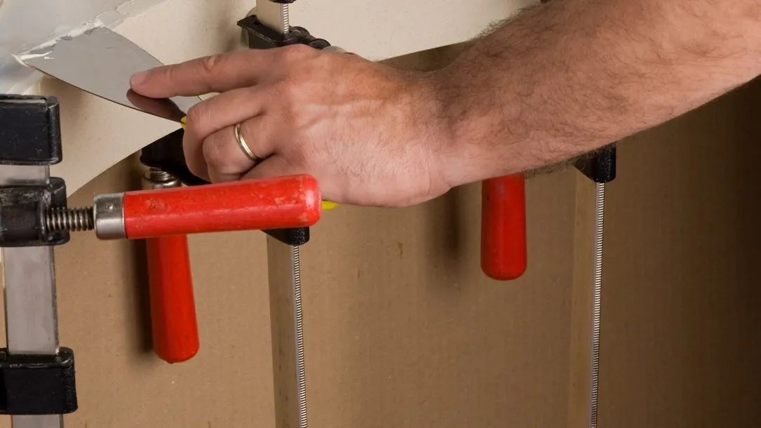 Fabricator applying adhesive to a curved Caesarstone quartz surface held by clamps during the thermoforming process.