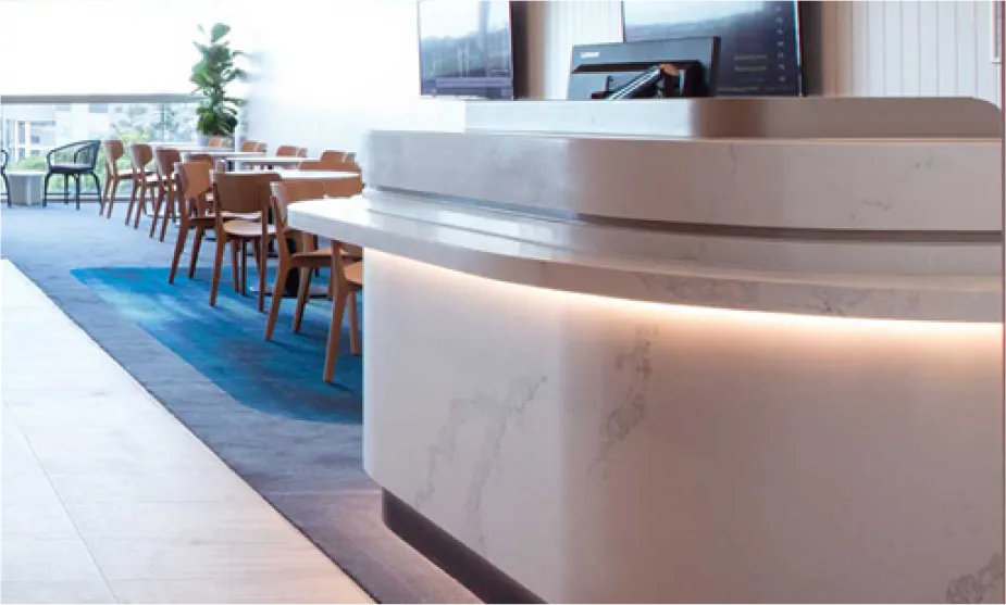 Curved white Caesarstone quartz reception counter with soft lighting in a modern office or dining space, demonstrating thermoformed surface design.