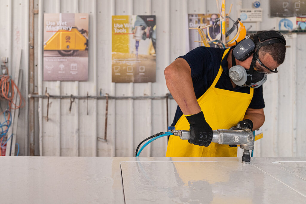 Fabrication & installation guide cover with Worker wearing protective gear and yellow apron uses power tool on a white surface.