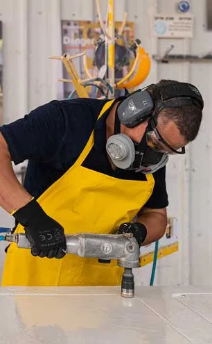 Fabrication & installation guide cover with Worker wearing protective gear and yellow apron uses power tool on a white surface.
